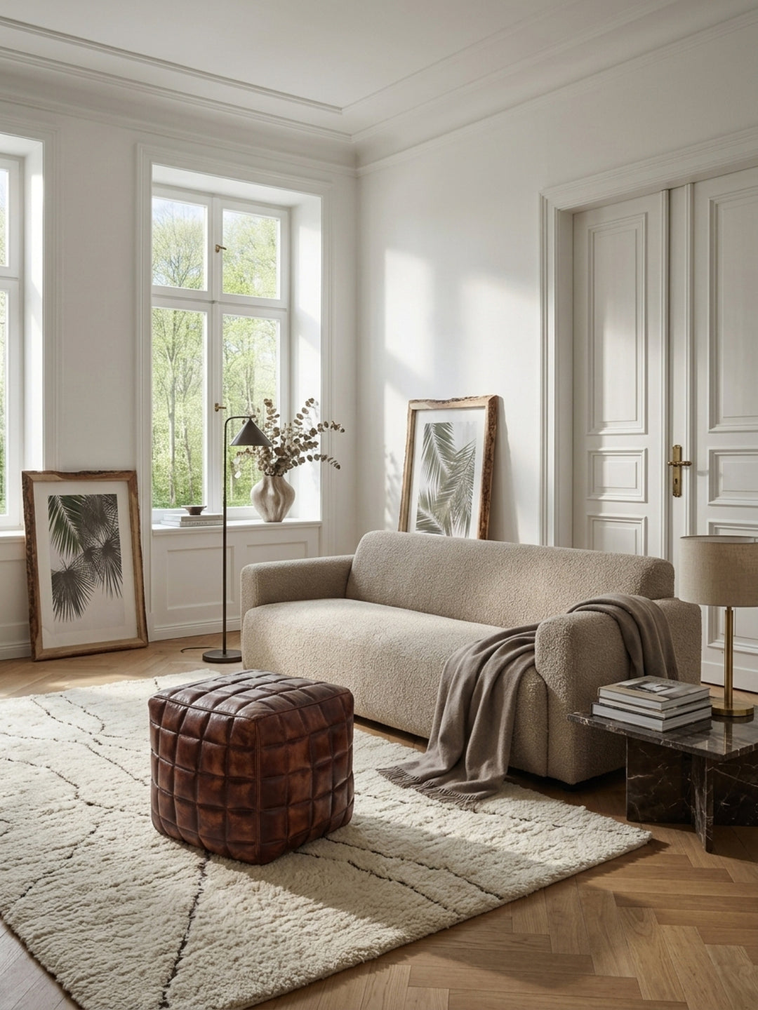 Ein eleganter Sitzwürfel aus braunem Echtleder steht in einem hellen Wohnzimmer im Modern-Classic-Stil auf einem cremefarbenen Teppich neben einem gemütlichen Lesesessel._