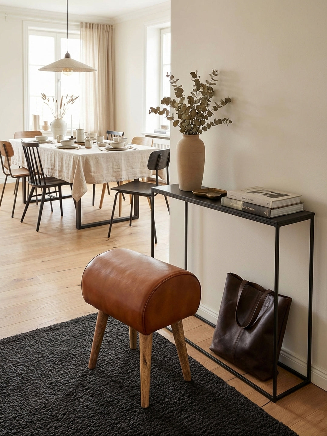 Moderner Sitzhocker im Turnbock-Stil mit cognac-braunem Echtleder in einem eleganten Eingangsbereich mit Holzboden und Design-Akzenten._