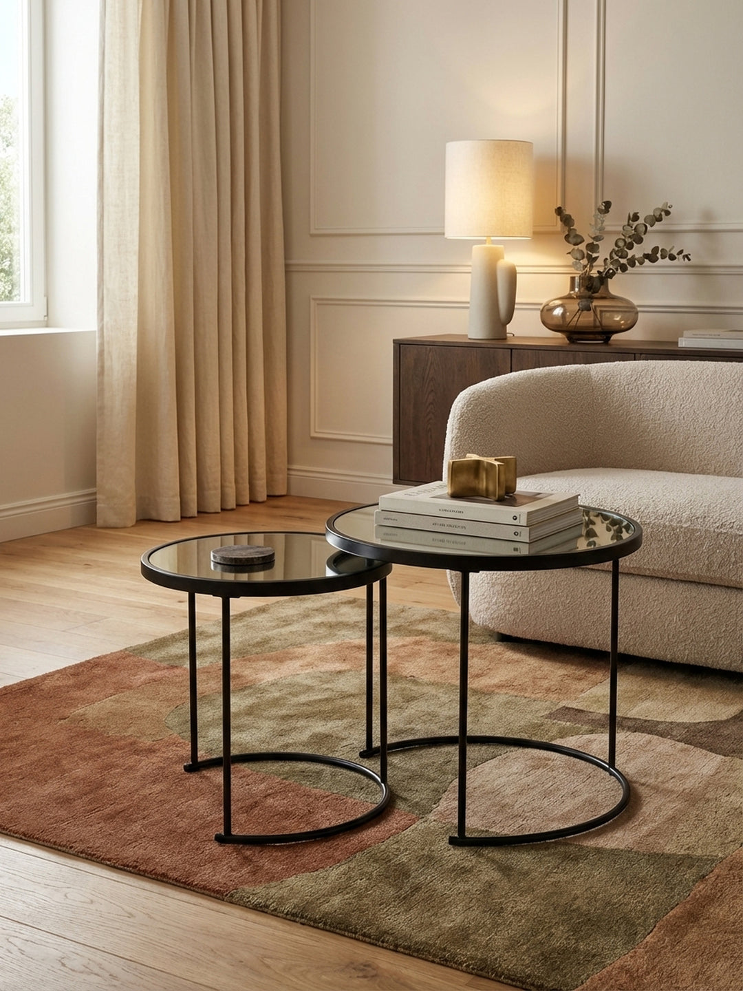 Modernes Satztisch-Set aus schwarzem Metall und Spiegelglas, elegant inszeniert neben einem grauen Sofa auf einem texturierten Teppich im Wohnzimmer._