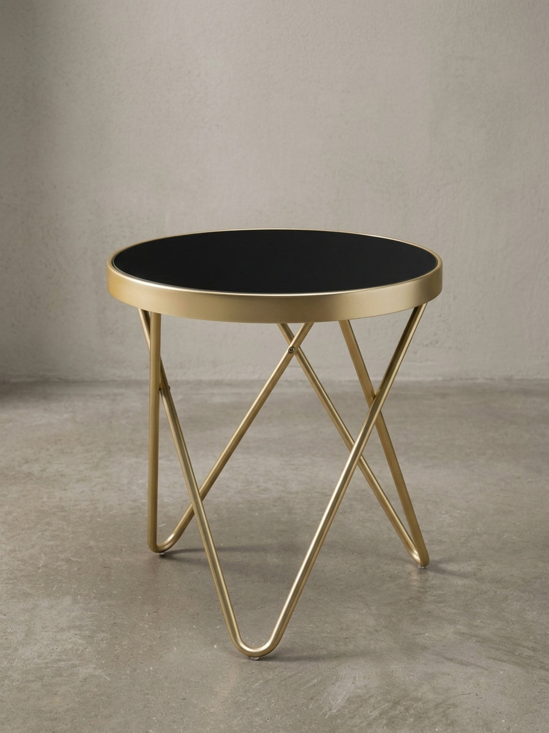 Runder Designer Beistelltisch PARMA frontal. Schwarzes Sicherheitsglas und ein matt-goldenes Gestell aus gekreuzten Streben vereinen sich zu einem 46 cm hohen, eleganten Möbelstück._