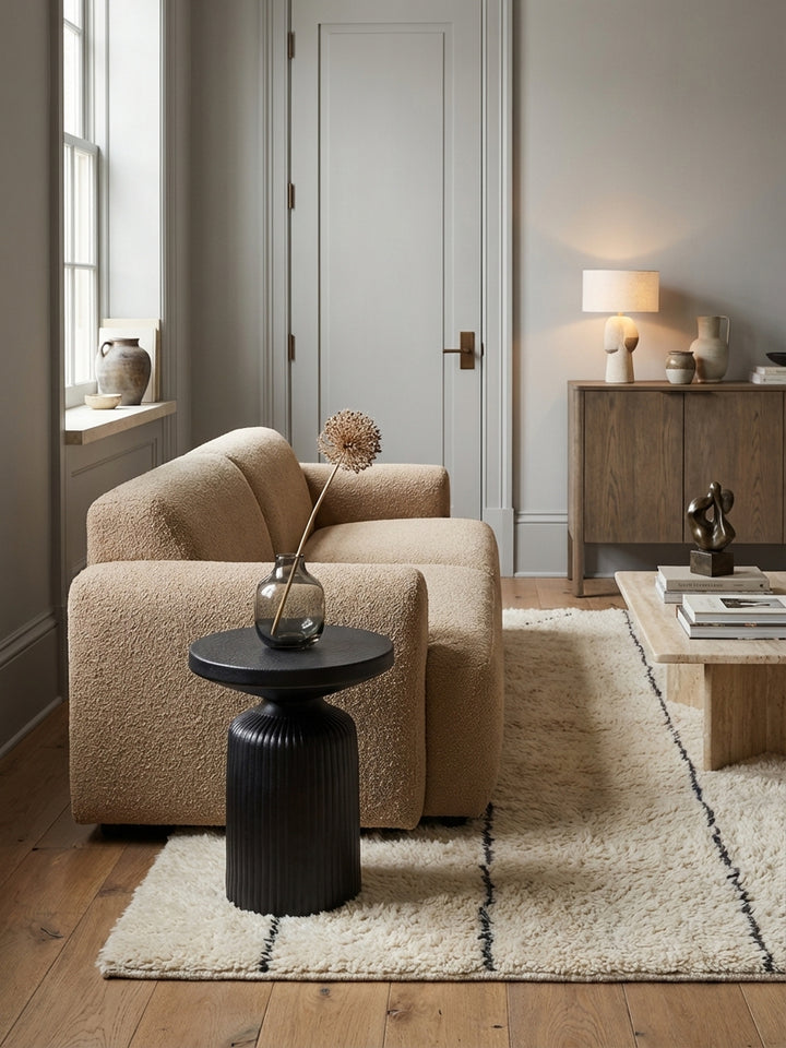 Runder Anstelltisch aus schwarzem Aluminium von oben gesehen, arrangiert mit Magazin und Pflanze auf einem hellen Holzboden im Wohnzimmer._