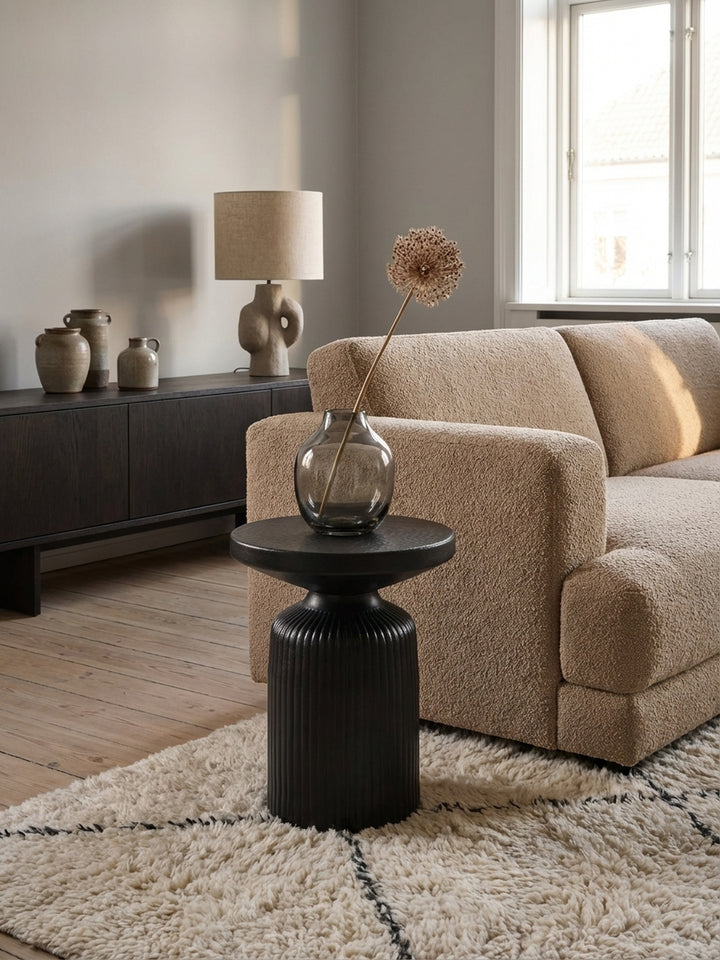 Einrichtungsidee mit dem schwarzen Beistelltisch, auf dem ein modernes Magazin und eine grüne Pflanze neben einem gemütlichen Sofa platziert sind._