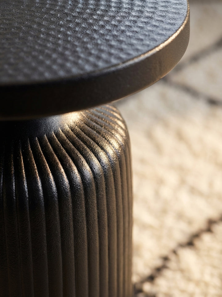 Detailaufnahme der Hammerschlag-Struktur auf der Oberfläche des runden, schwarzen Metall-Beistelltisches, die handgefertigte Qualität zeigend._