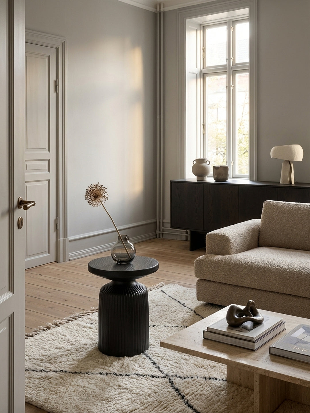 Skulpturaler schwarzer Beistelltisch aus Metall neben einem beigen Sofa in einem hellen, modern-minimalistischen Wohnzimmer mit Holzboden._