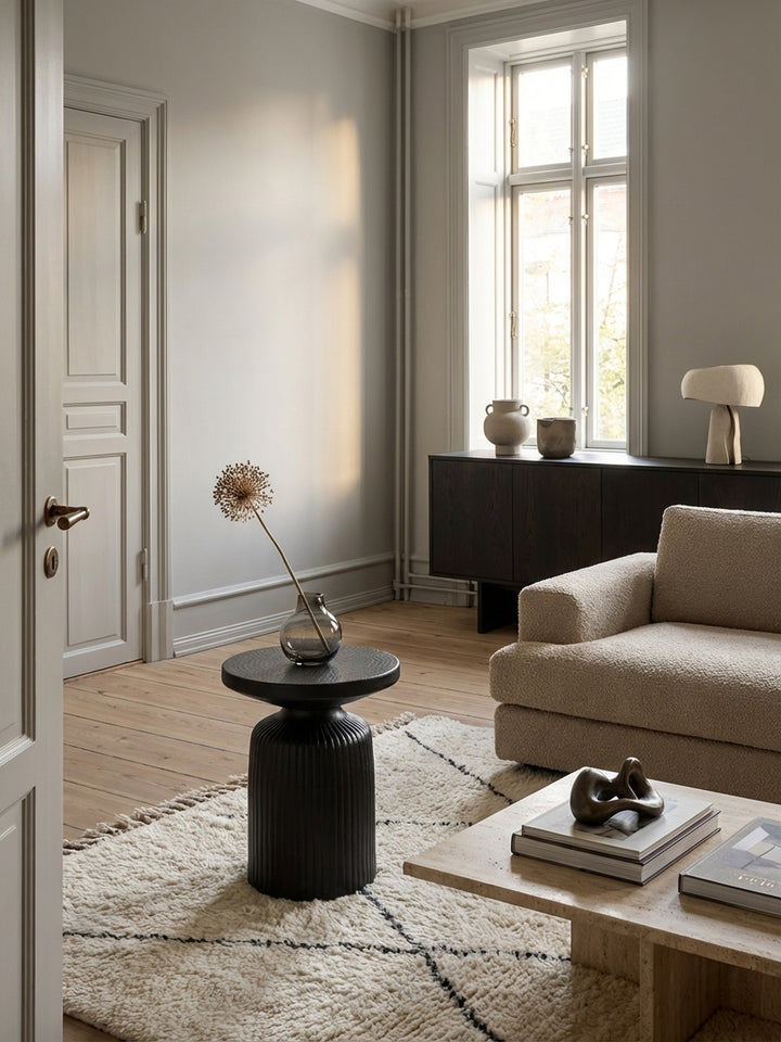 Skulpturaler schwarzer Beistelltisch aus Metall neben einem beigen Sofa in einem hellen, modern-minimalistischen Wohnzimmer mit Holzboden._