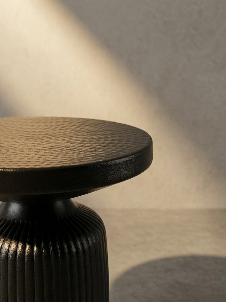 Alternativ-Perspektive des schwarzen Design-Beistelltisches, die das Zusammenspiel von glatter Kante und texturierter Oberfläche verdeutlicht._