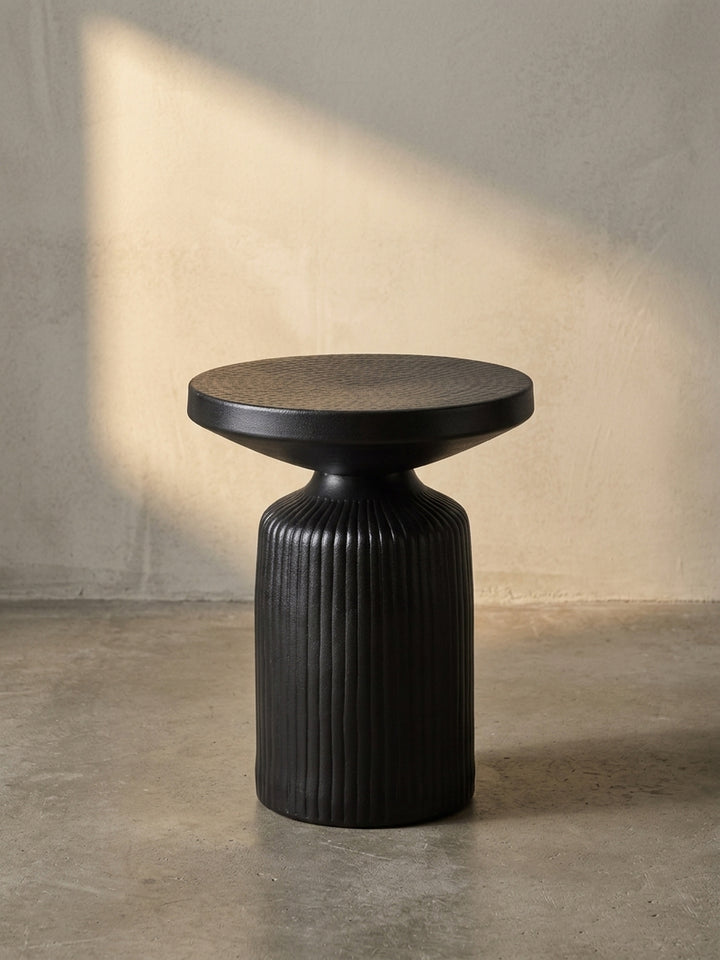 Frontansicht des handgefertigten Beistelltisches aus Aluminium in Schwarz, dessen gerillter Standfuß und gehämmerte Platte gut sichtbar sind._