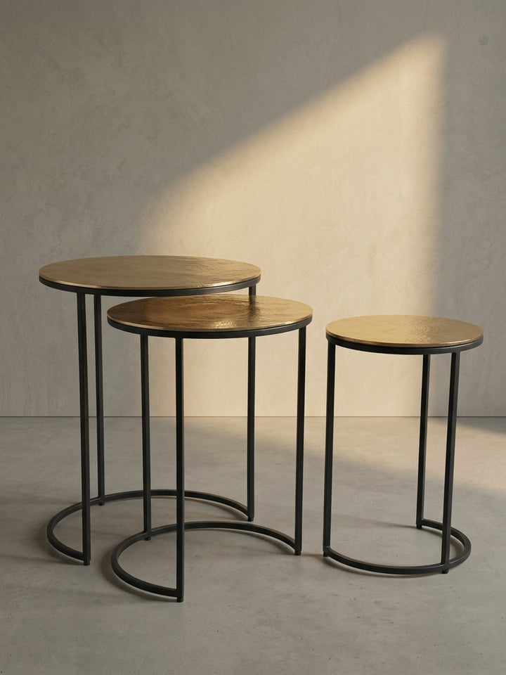 Schräge 3/4-Ansicht des dreiteiligen Satztisches, die die elegante Form des schwarzen Metallgestells und die goldenen Platten hervorhebt._