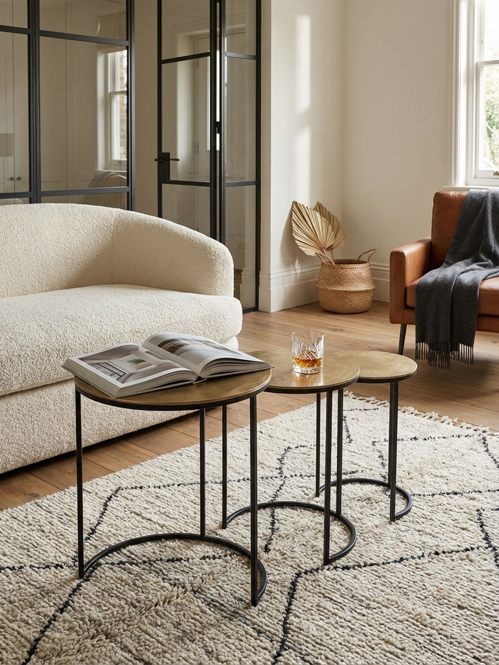 Draufsicht auf einen goldenen Satztisch aus Metall, der als Couchtisch mit Pflanze und Glas auf einem strukturierten Berberteppich dekoriert ist._