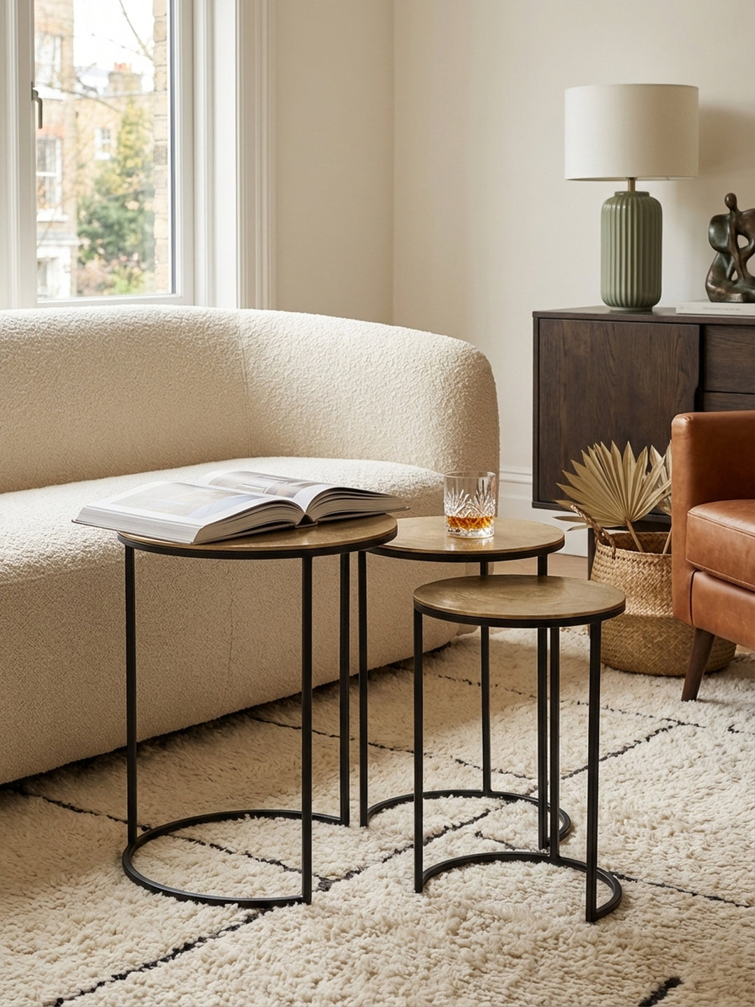 Das dreiteilige Beistelltisch-Set aus goldfarbenem Aluminium und schwarzem Metall als flexible Ablage im modernen Wohnzimmer._