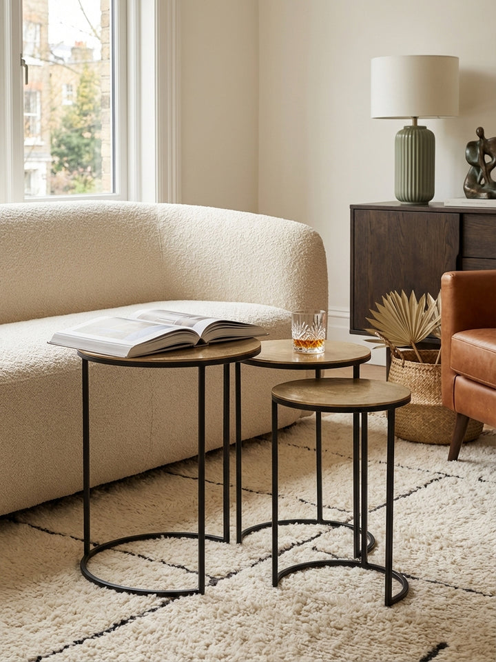 Das dreiteilige Beistelltisch-Set aus goldfarbenem Aluminium und schwarzem Metall als flexible Ablage im modernen Wohnzimmer._