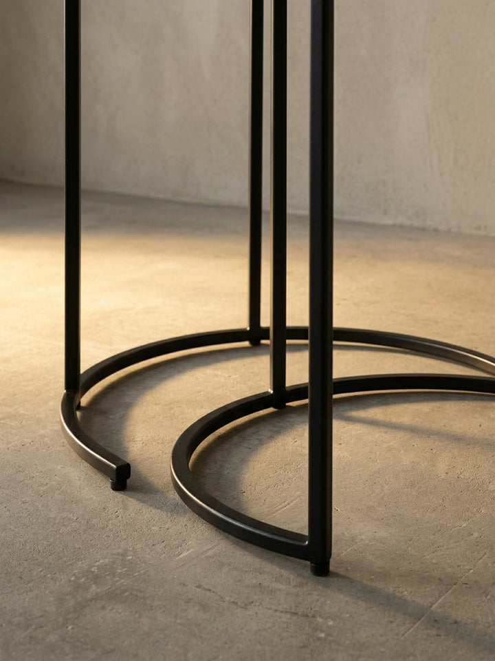 Nahaufnahme der Kante einer goldenen Tischplatte, die auf dem filigranen, mattschwarzen Eisengestell des modernen Abstelltisches ruht._