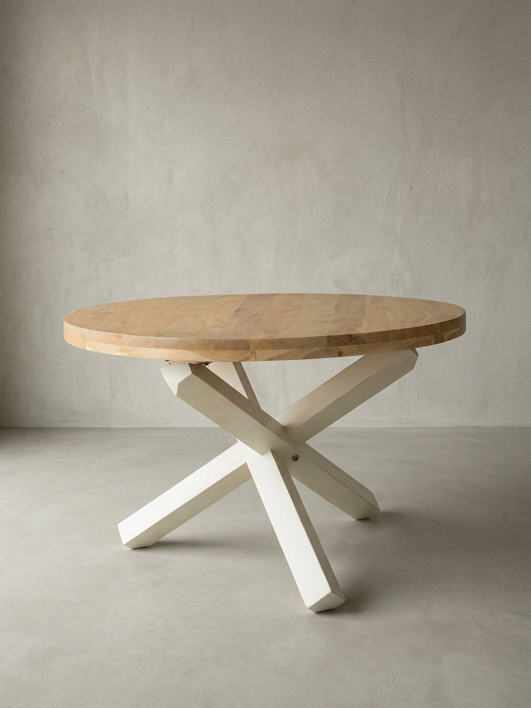 Freigestellter runder Esstisch im modernen Landhausstil. Die frontale Ansicht zeigt die braune Massivholzplatte aus Akazie und das markante dreibeinige Kreuzgestell in Cremeweiß._