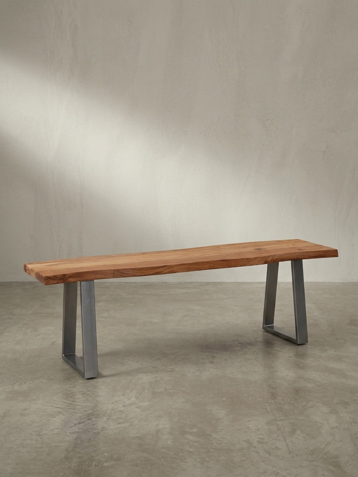Schräge 3/4-Ansicht der 120x40 cm großen Massivholzbank, die die Tiefe der Sitzfläche aus Akazie und die glänzenden Metallkufen hervorhebt._