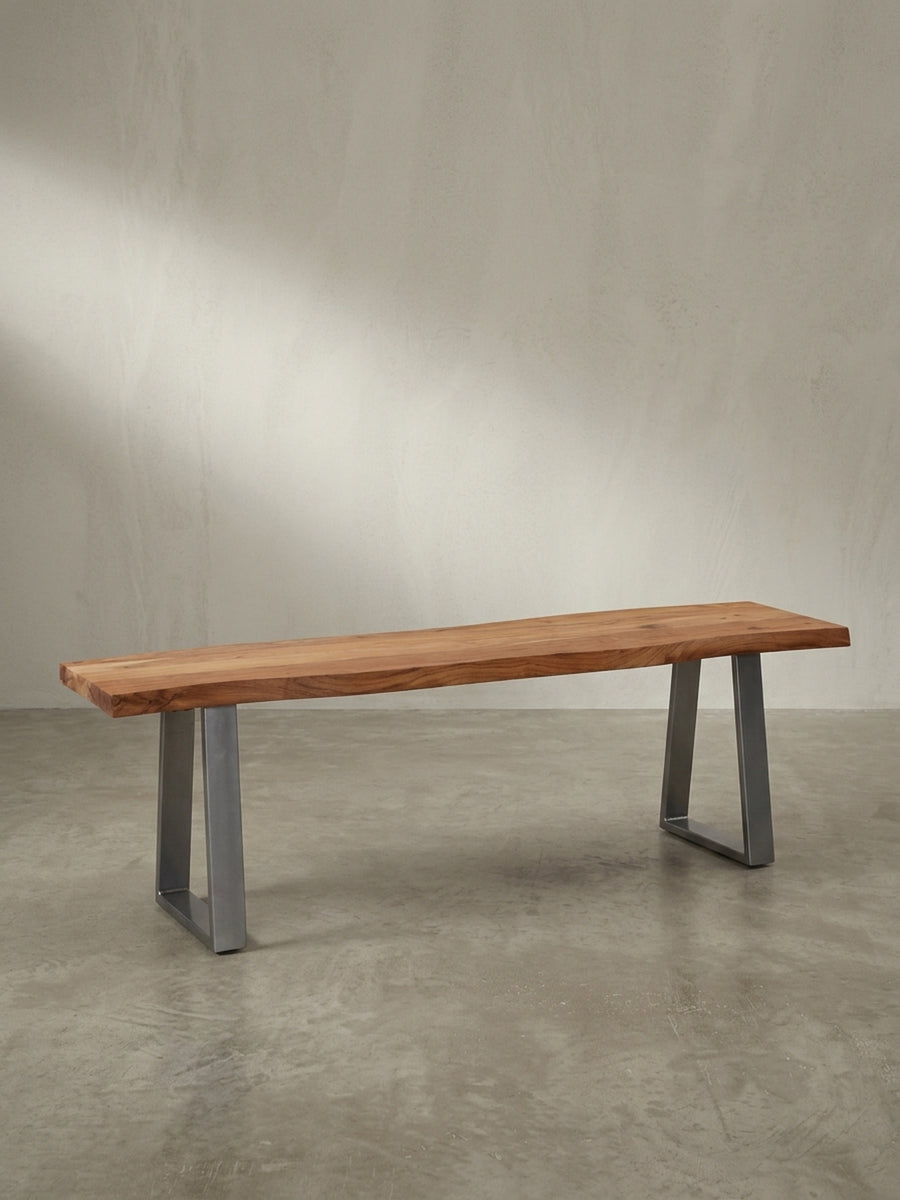 Schräge 3/4-Ansicht der 120x40 cm großen Massivholzbank, die die Tiefe der Sitzfläche aus Akazie und die glänzenden Metallkufen hervorhebt._