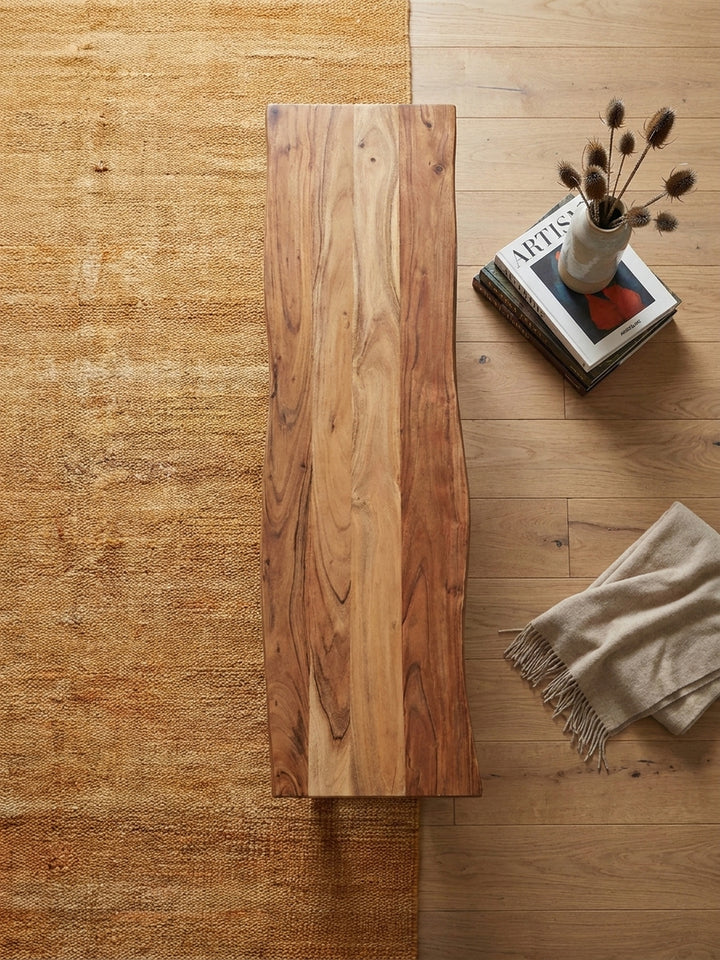 Draufsicht auf eine 120 cm lange Holzbank aus Akazie neben einem Esstisch auf einem Vintage-Teppich, die die klare Linienführung im Raum zeigt._