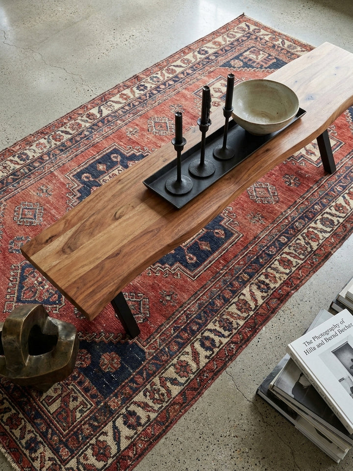 Draufsicht auf eine massive Holzbank aus Akazie mit Metallbeinen, die zusammen mit einem Esstisch auf einem Vintage-Kelim-Teppich steht._