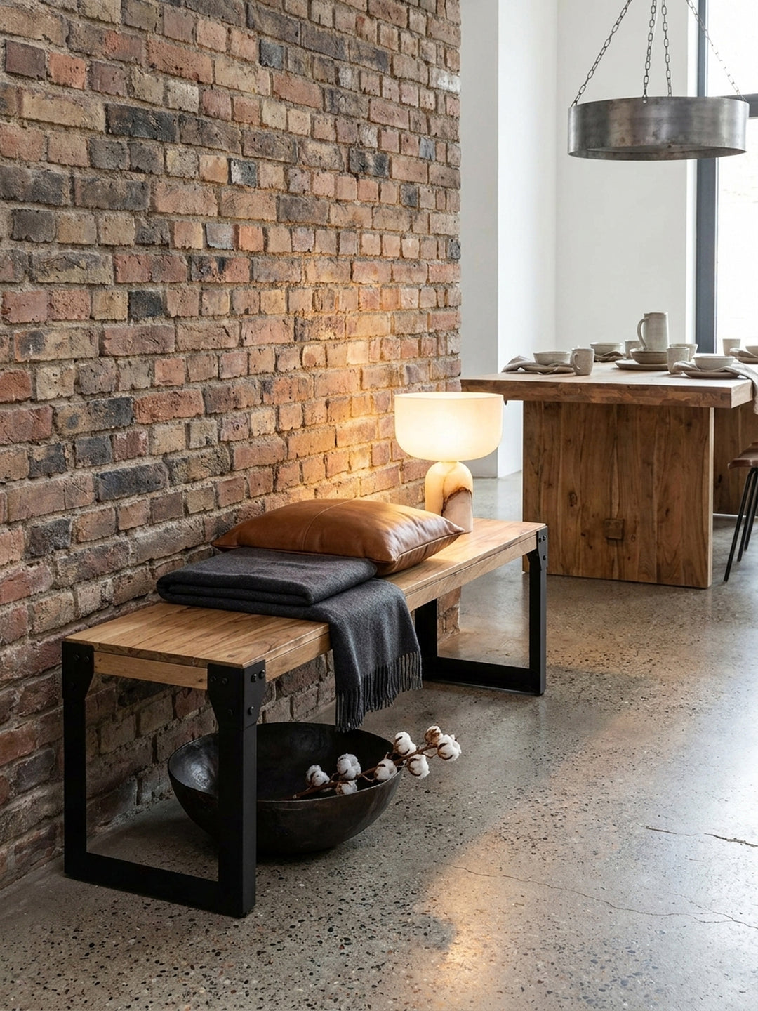 Ein gelbes Wolltuch liegt auf der Sitzbank aus Akazienholz und Metall und schafft eine gemütliche Atmosphäre im Esszimmer._