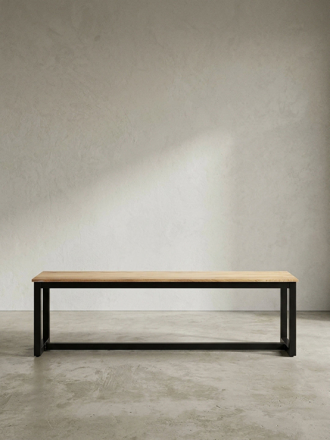 Gerade Frontalansicht der minimalistischen Esszimmerbank 120 cm breit, mit Sitzfläche aus heller Akazie und einem Gestell aus schwarzem Eisen._