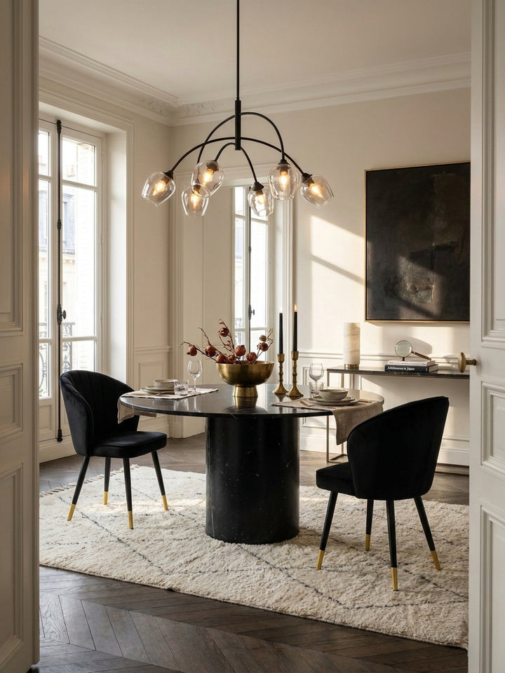 Elegantes Esszimmer mit einem luxuriösen Schalenstuhl aus schwarzem Samt auf dunklem Fischgrätparkett unter einer filigranen Messingpendelleuchte._