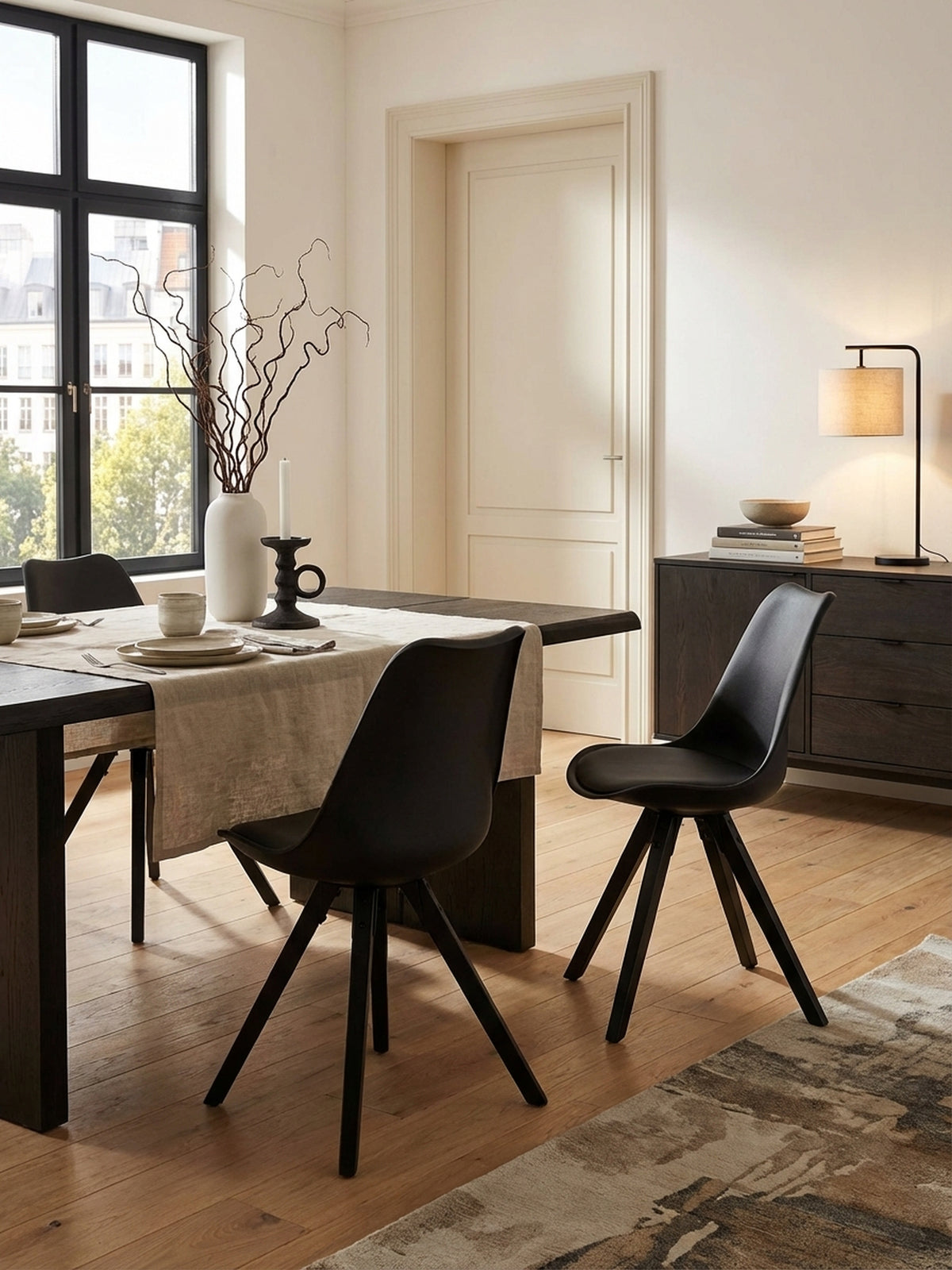 Zwei schwarze Esszimmerstühle im Skandi-Stil an einem Holztisch in einem hellen, modernen Esszimmer, unterstreichen ein minimalistisches Wohnkonzept.