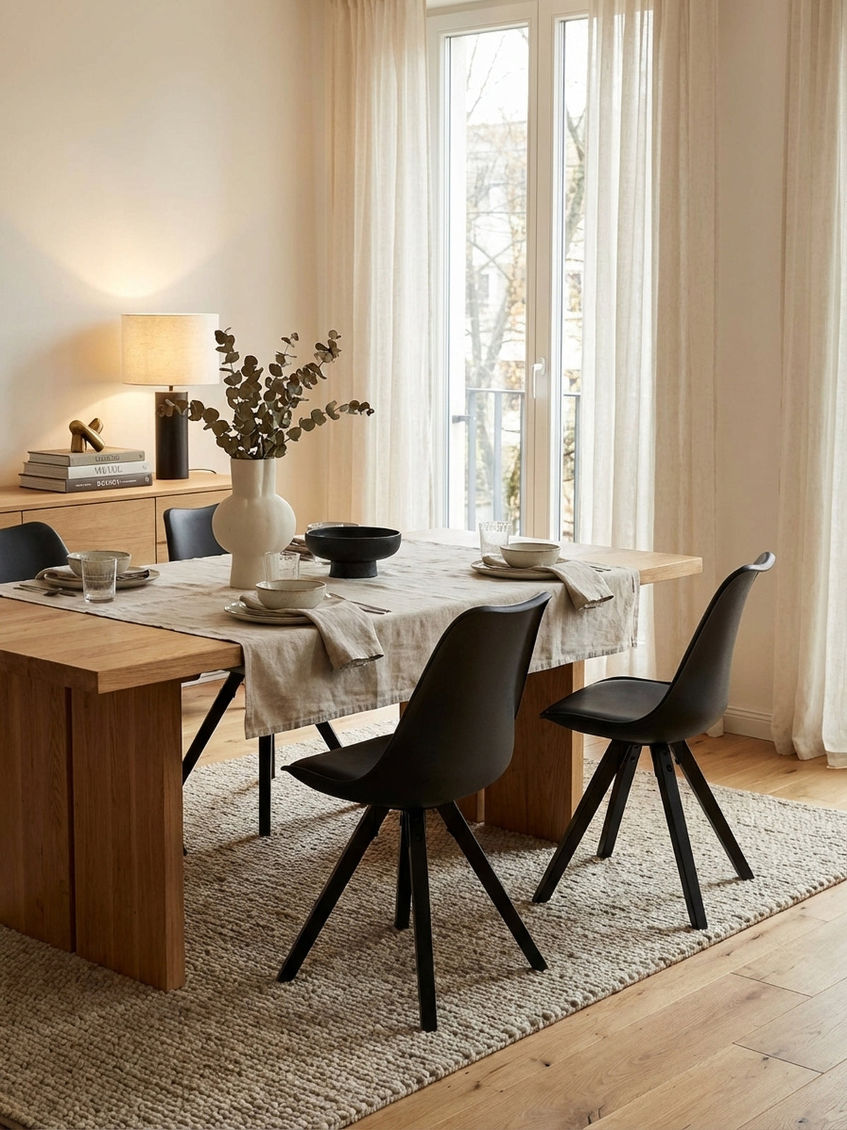 Draufsicht auf ein Esszimmer-Ensemble mit vier schwarzen Schalenstühlen um einen runden Tisch auf einem beigen Wollteppich, zeigt eine harmonische Raumaufteilung._