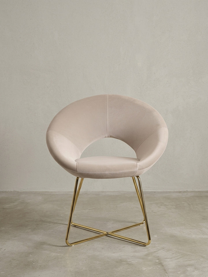 Esszimmerstuhl in Samt Beige aus der Dreiviertelperspektive, zeigt die geschwungene Sitzschale und die elegant gekreuzten goldenen Stuhlbeine._