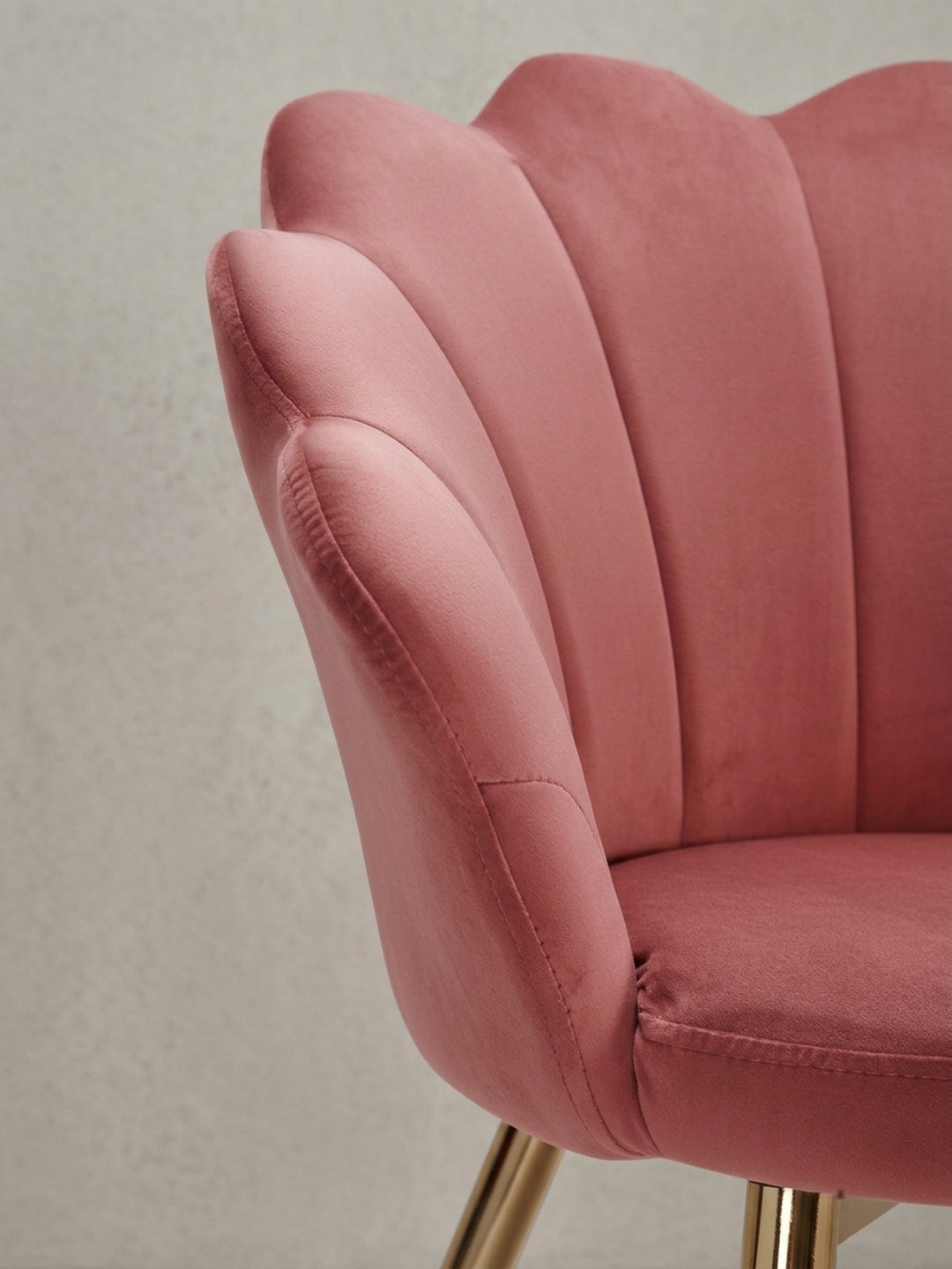 Perspektivische Ansicht des Design-Stuhls, die das Zusammenspiel von weichem rosa Samtbezug und glänzend goldenen Beinen unterstreicht._