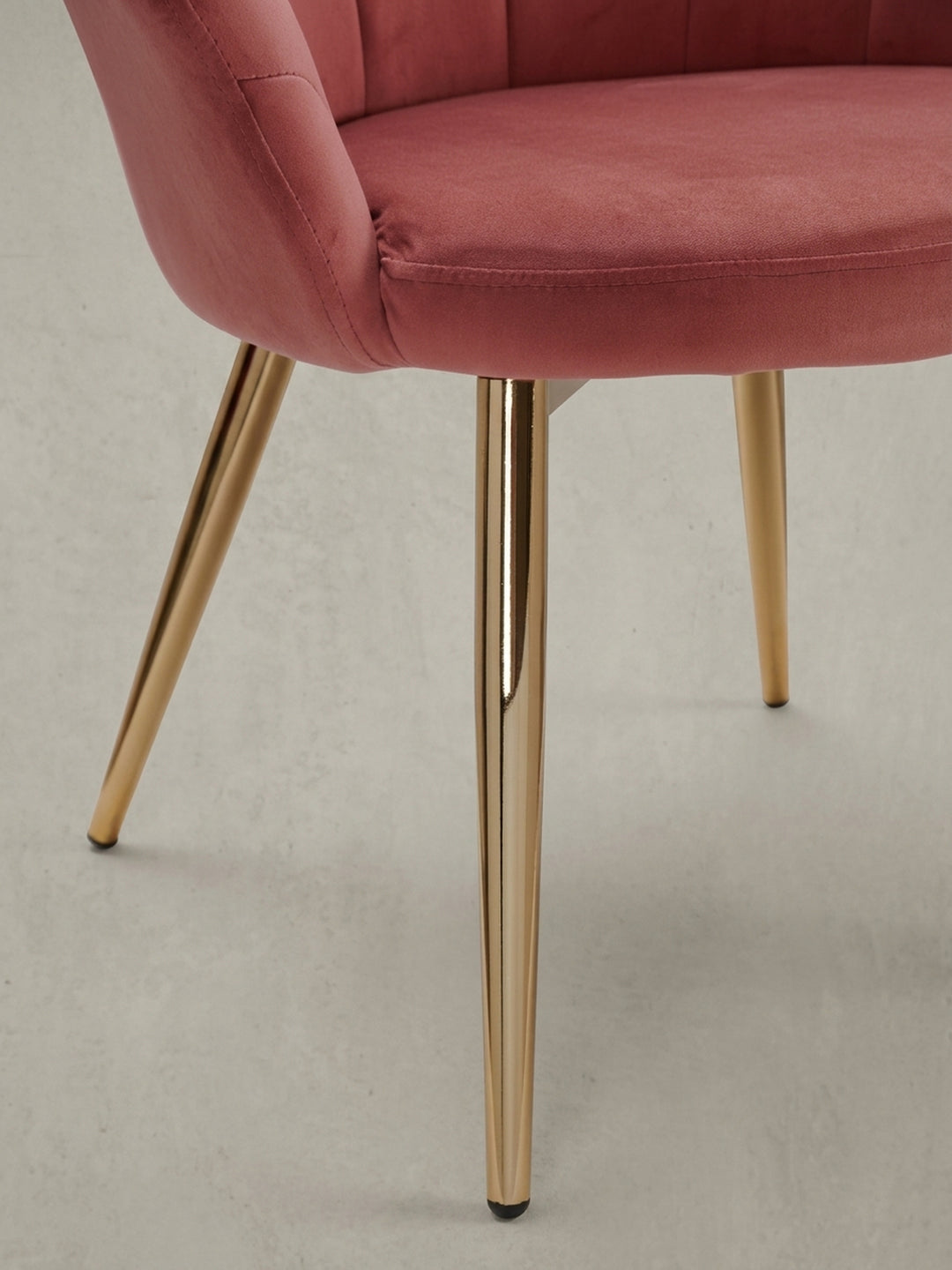 Detailaufnahme der schlanken, goldfarbenen Stuhlbeine und des Übergangs zur weich gepolsterten Sitzschale aus rosa Samtstoff._