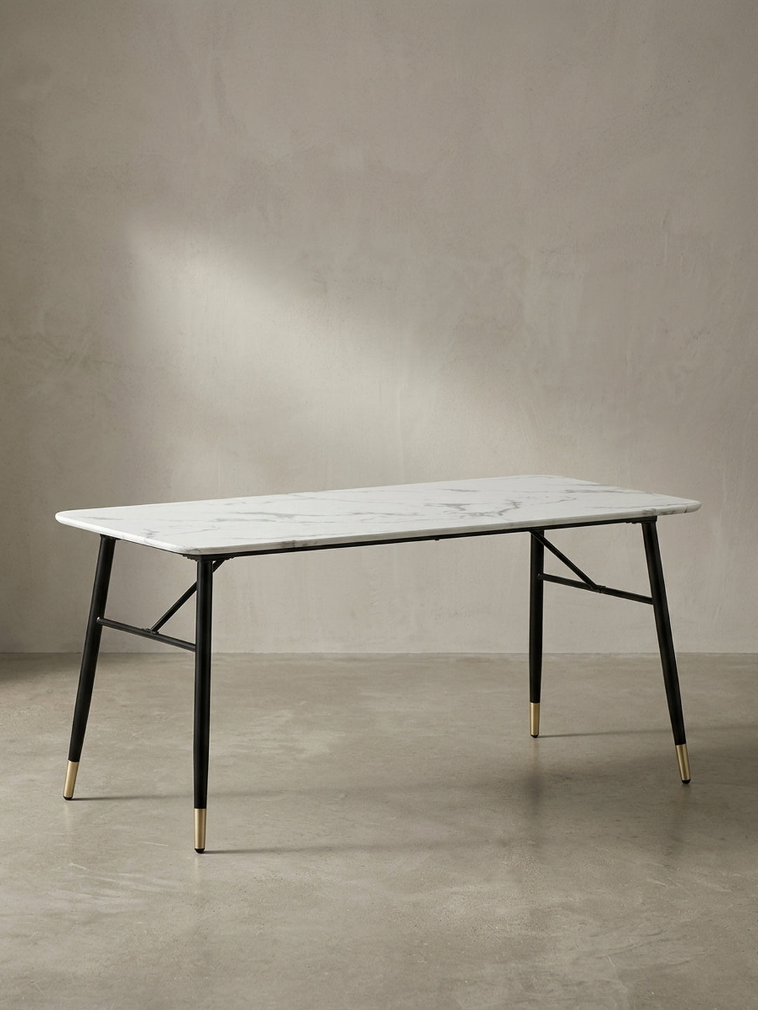 Freigestellter Esstisch 180x90x76 cm in weißer Marmor-Optik mit ausgestellten schwarzen Eisenbeinen und messingfarbenen Füßen in der Frontalansicht_