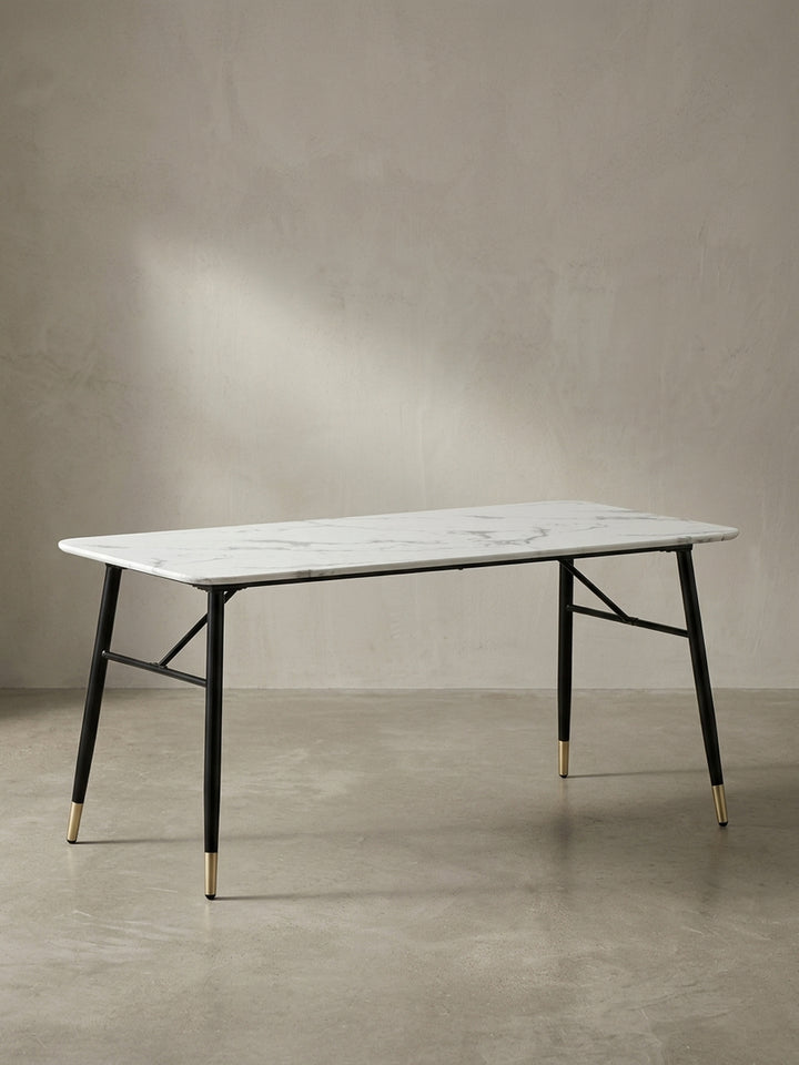 Freigestellter Esstisch 180x90x76 cm in weißer Marmor-Optik mit ausgestellten schwarzen Eisenbeinen und messingfarbenen Füßen in der Frontalansicht_