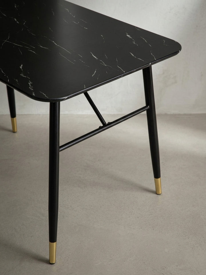 Detaillierte Sicht auf die glänzenden, goldfarbenen Fußenden des schwarzen Metallgestells an dem modernen Tisch im Marmor-Look_