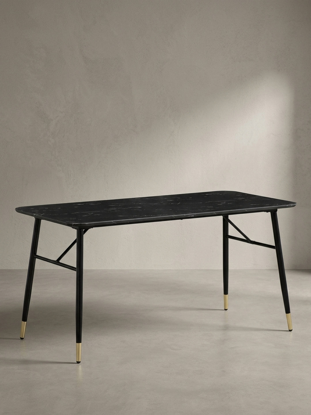 Moderner Esszimmertisch schräg von links betrachtet zeigt die X-förmigen Querstreben des schwarzen Metallgestells und die eleganten goldenen Fußabschlüsse_