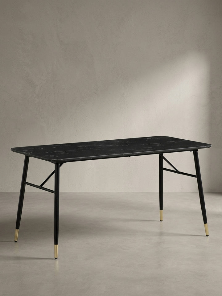 Moderner Esszimmertisch schräg von links betrachtet zeigt die X-förmigen Querstreben des schwarzen Metallgestells und die eleganten goldenen Fußabschlüsse_