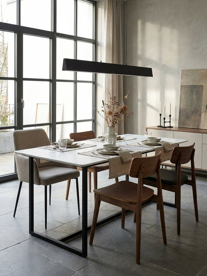 Minimalistischer Esstisch mit schwarzem Kufengestell und weißer Marmorplatte kombiniert mit eleganten Esszimmerstühlen vor einer grauen Betonwand._
