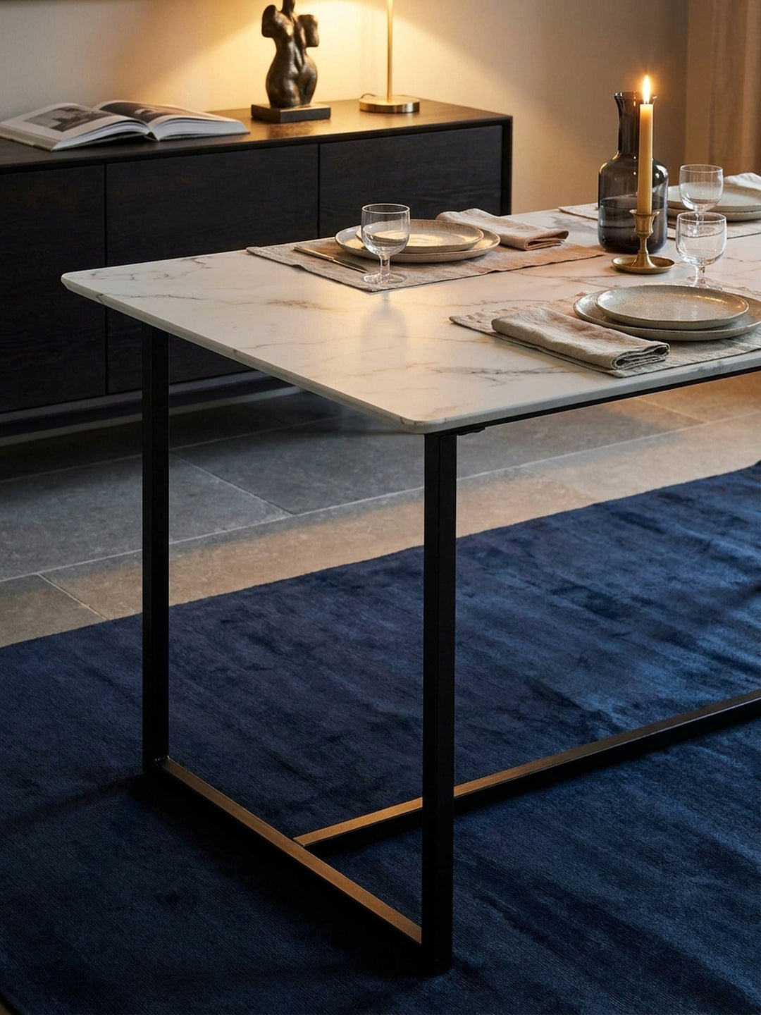 Gedeckter Esszimmertisch im modernen Marmor-Look mit einer Rauchglaskaraffe und Calacatta Viola Tablett beleuchtet von einer linearen Pendelleuchte._