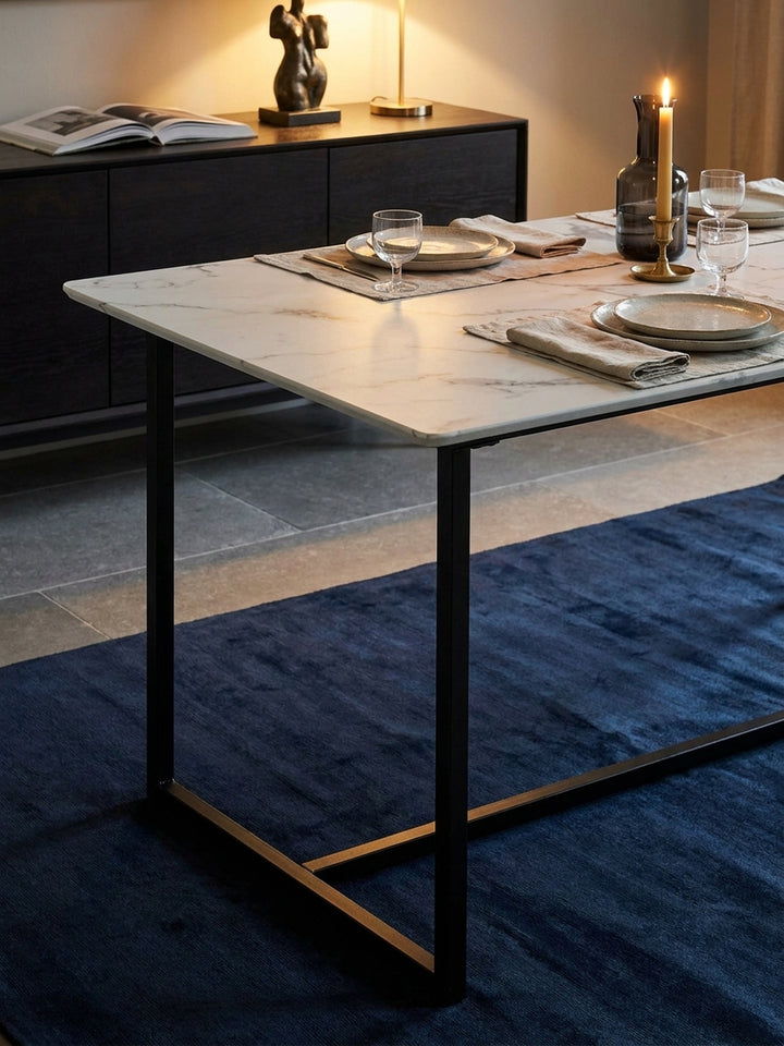 Gedeckter Esszimmertisch im modernen Marmor-Look mit einer Rauchglaskaraffe und Calacatta Viola Tablett beleuchtet von einer linearen Pendelleuchte._