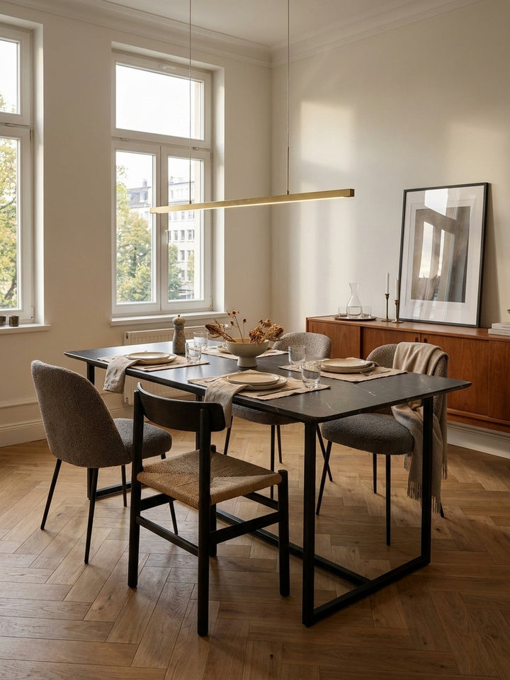 Design Esstisch mit schwarzen Eisenbeinen kombiniert mit modernen Polsterstühlen in Grau unter einer linearen Messing Pendelleuchte_