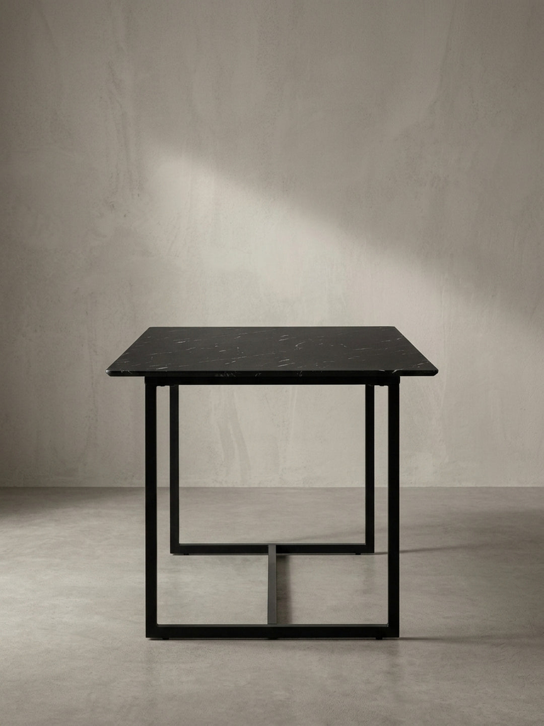 Eleganter Esstisch mit durchgehender Bodenstrebe am schwarzen Metallgestell freigestellt in Schrägansicht von der rechten Seite_