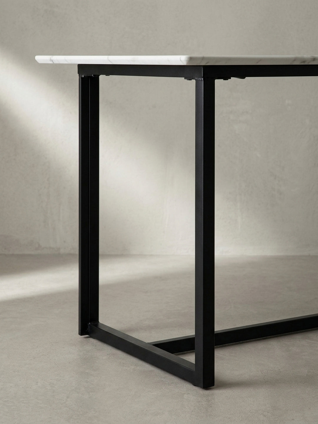 Makroaufnahme der perfekten Verbindungsstellen zwischen der glänzenden Tischplatte im Marmor-Design und dem mattschwarzen Eisenprofil des Tischgestells_