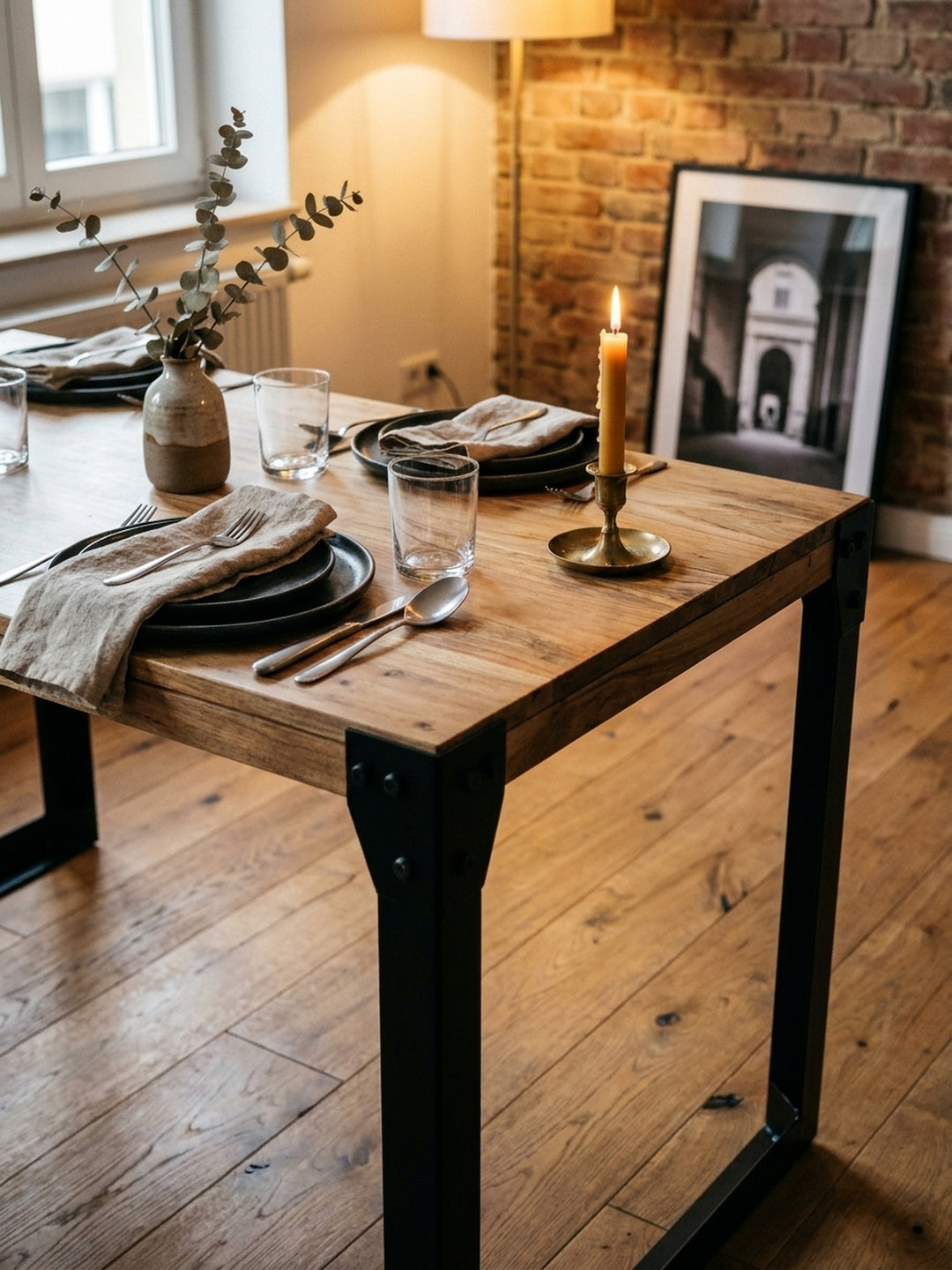 Ein gemütliches Abendessen-Setting auf dem Akazien-Esstisch mit dunklem Keramikgeschirr und einer Vase, das die warme Atmosphäre des Industrial Designs unterstreicht._