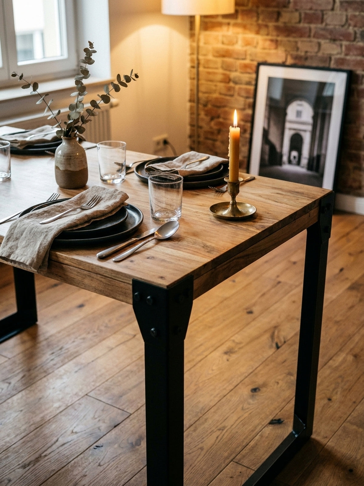 Ein gemütliches Abendessen-Setting auf dem Akazien-Esstisch mit dunklem Keramikgeschirr und einer Vase, das die warme Atmosphäre des Industrial Designs unterstreicht._