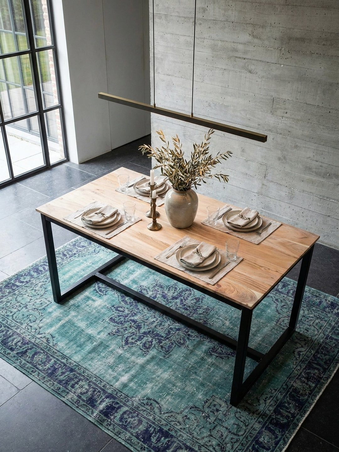 Draufsicht auf den rechteckigen Esszimmertisch aus Akazie im Industrial Style, umgeben von eleganten Polsterstühlen auf einem blauen Vintage Teppich im weitläufigen Wohnbereich._