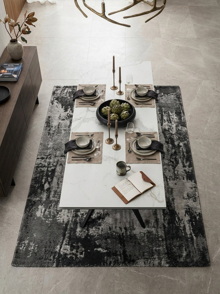 Draufsicht auf den Designer-Esstisch mit weißer Keramikplatte und schwarzen Metallbeinen, umgeben von Samtstühlen auf Kalksteinboden._