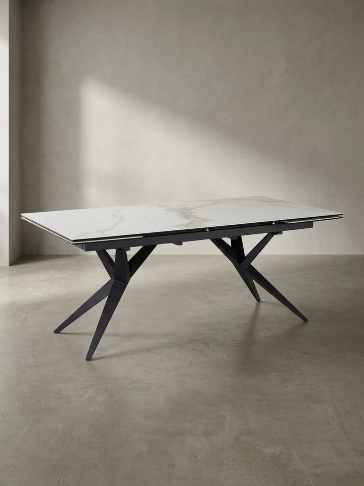 Designer-Esstisch aus Keramik und Metall in einer schrägen 3/4-Ansicht, die die filigrane Tischplatte und das massive Gestell zeigt._