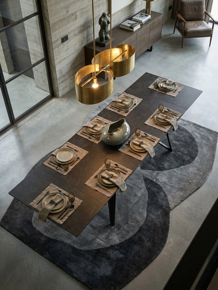 Blick von oben auf den modernen Keramiktisch mit extravagantem Metallgestell, umgeben von vier Stühlen auf einem beigen Teppich in einem lichtdurchfluteten Raum._