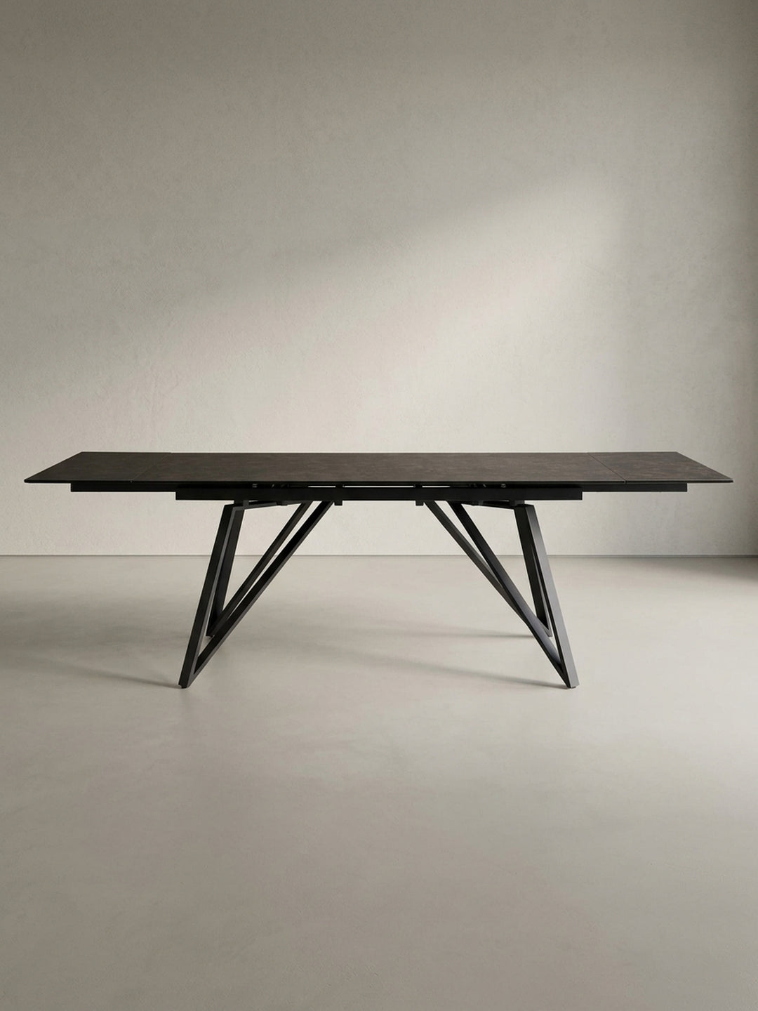 Der große Designer-Esstisch in 3/4-Ansicht, der die filigrane Tischplatte und das robuste, geometrische Beingestell aus Eisen eindrucksvoll zur Geltung bringt._