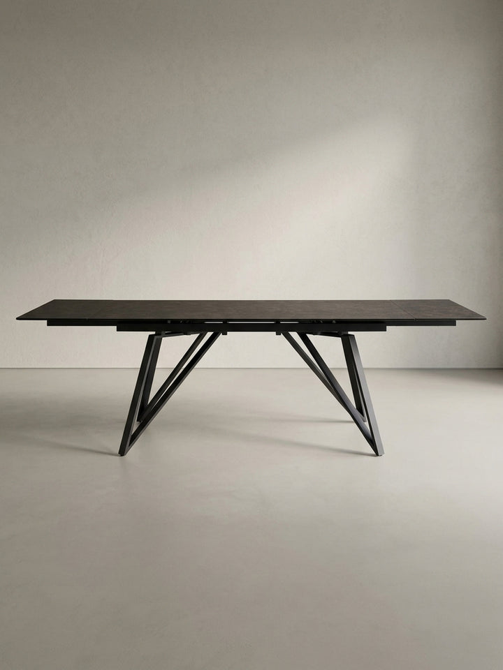 Der große Designer-Esstisch in 3/4-Ansicht, der die filigrane Tischplatte und das robuste, geometrische Beingestell aus Eisen eindrucksvoll zur Geltung bringt._