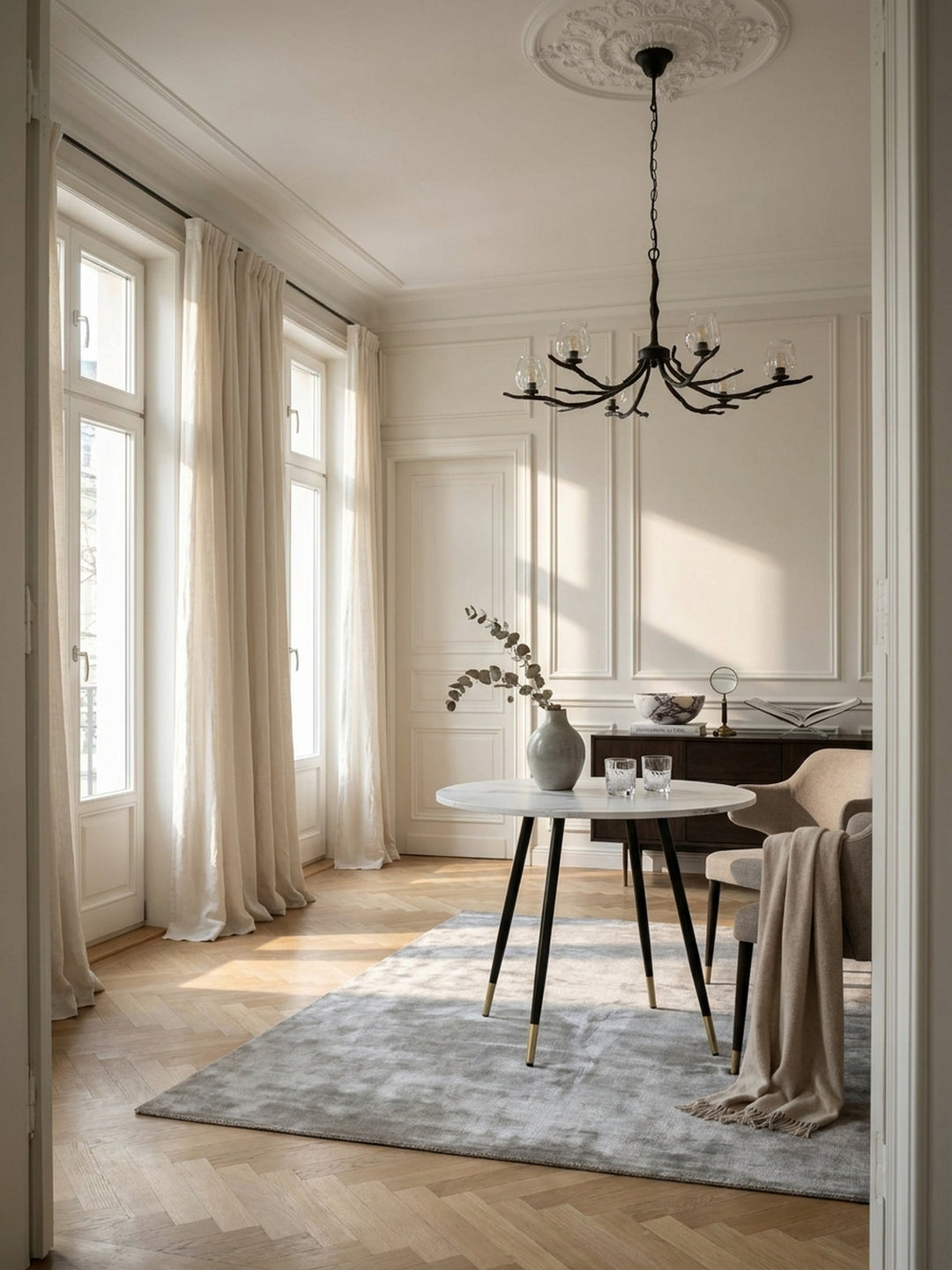 Eleganter runder Esstisch mit weißer Marmor-Optik und schwarzen Metallbeinen im großzügigen Pariser Altbau Esszimmer auf hellem Fischgrätparkett_