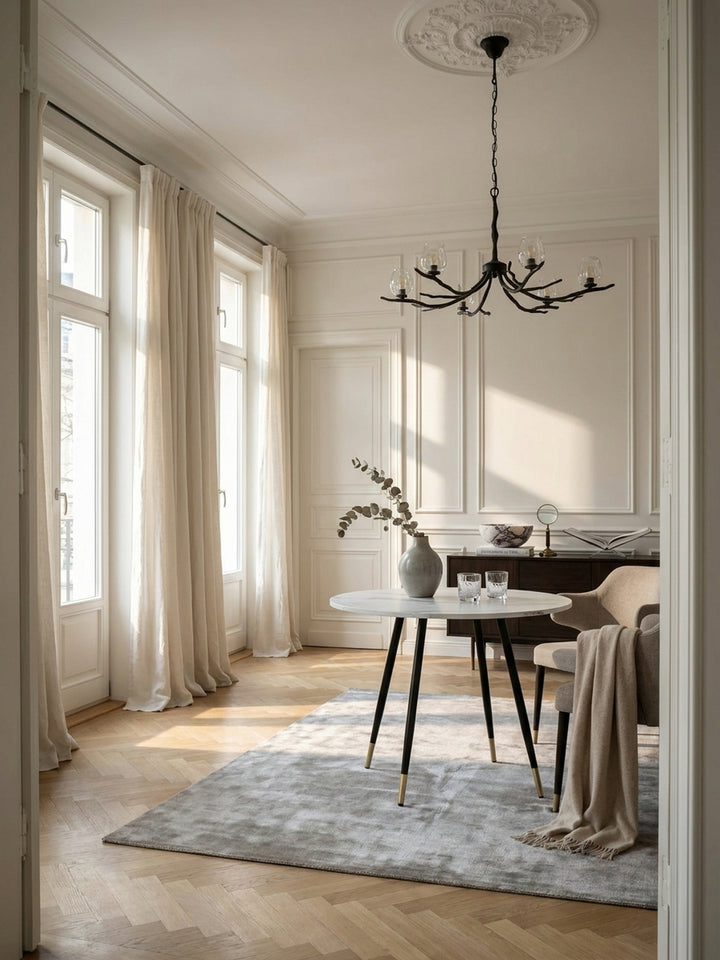 Eleganter runder Esstisch mit weißer Marmor-Optik und schwarzen Metallbeinen im großzügigen Pariser Altbau Esszimmer auf hellem Fischgrätparkett_